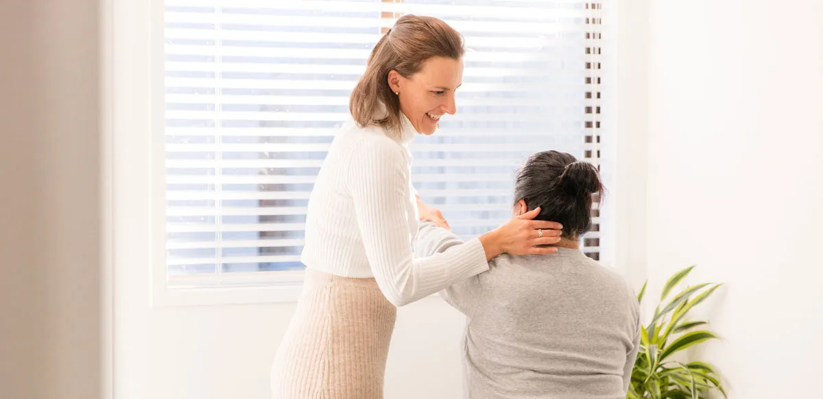 A chiropractor checking a seated patient's neck in a treatment room.