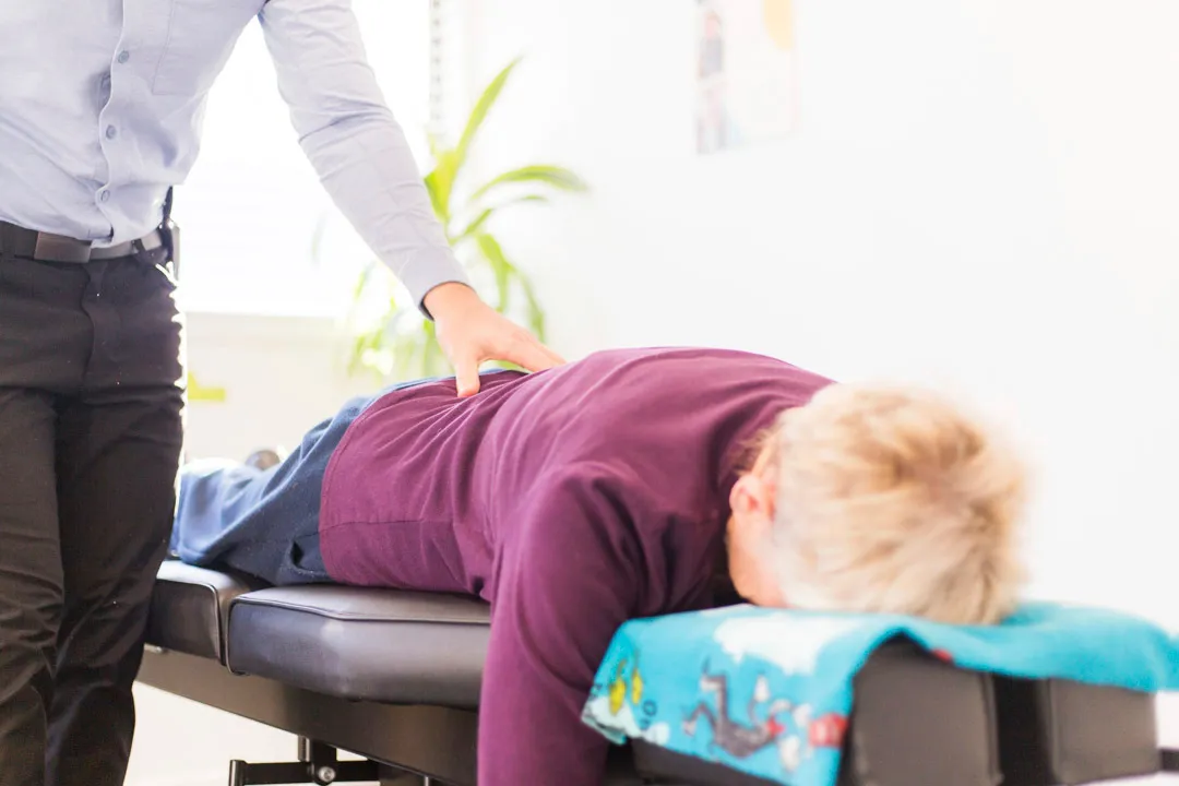 A chiropractor performing a spinal adjustment on a patient lying face down