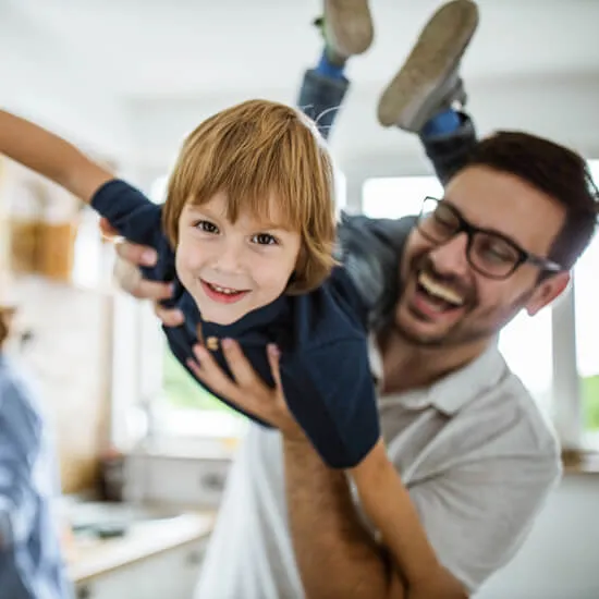 A father playfully lifting a laughing young boy over his head at home